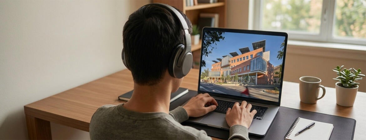 Male student with headphones working on a laptop that displays the UCR School of Business building