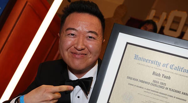 Rich Yueh smiling and pointing at his certificate for the Shulman Endowed Excellence in Teaching Award