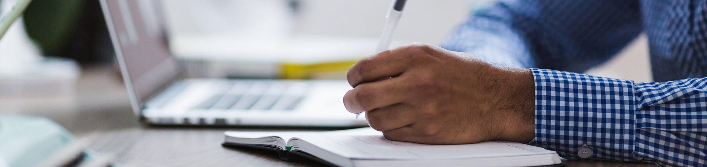Hand holding pencil on desk with laptop