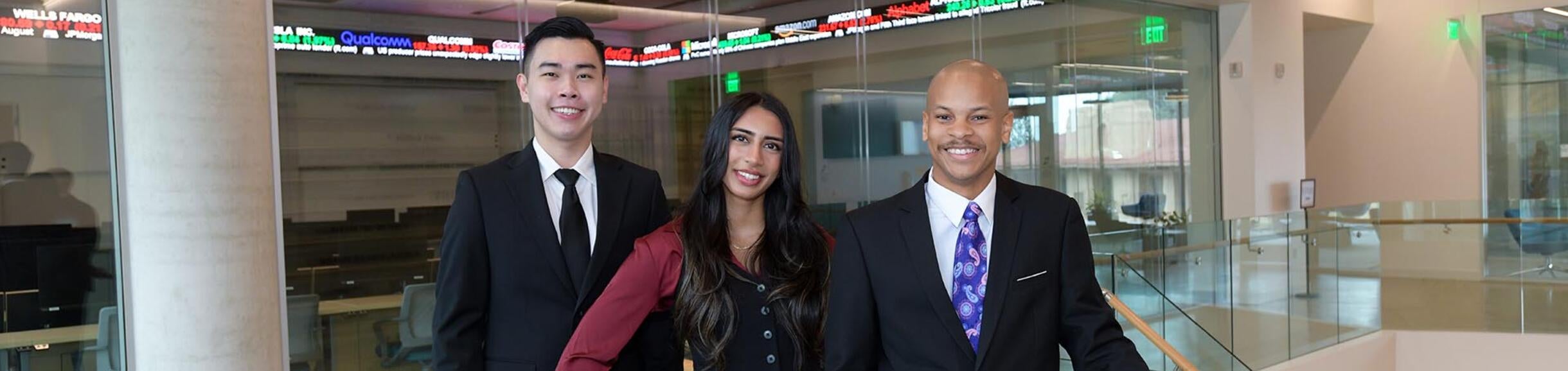 Three graduate students in front of the finance lab at the UC Riverside School of Business in California