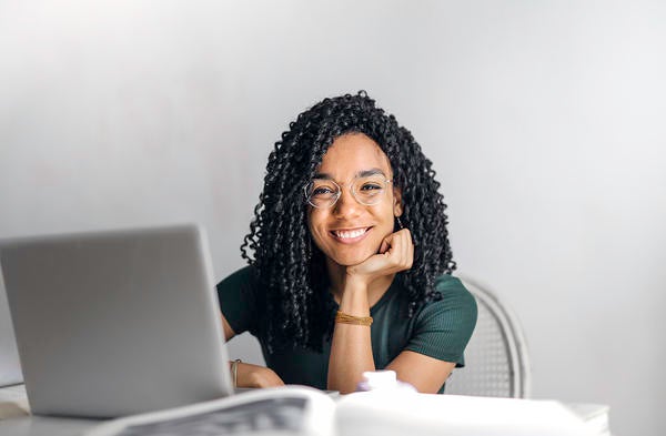 young woman smiling, sitting at laptop, chin on hand