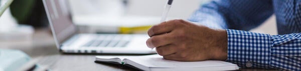 Hand holding pencil on desk with laptop