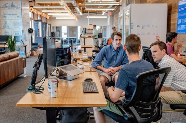 students conversing sitting at a table looking at computers (c) unsplash