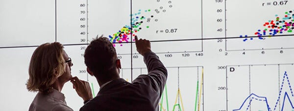 Two people in front of a digital dashboard showing Business Analytics data